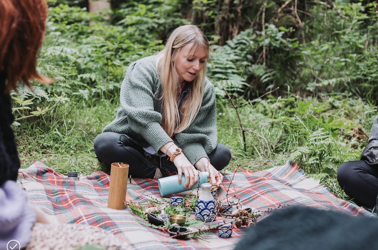 Forest retreat pouring herbal tea on a picnic blanket